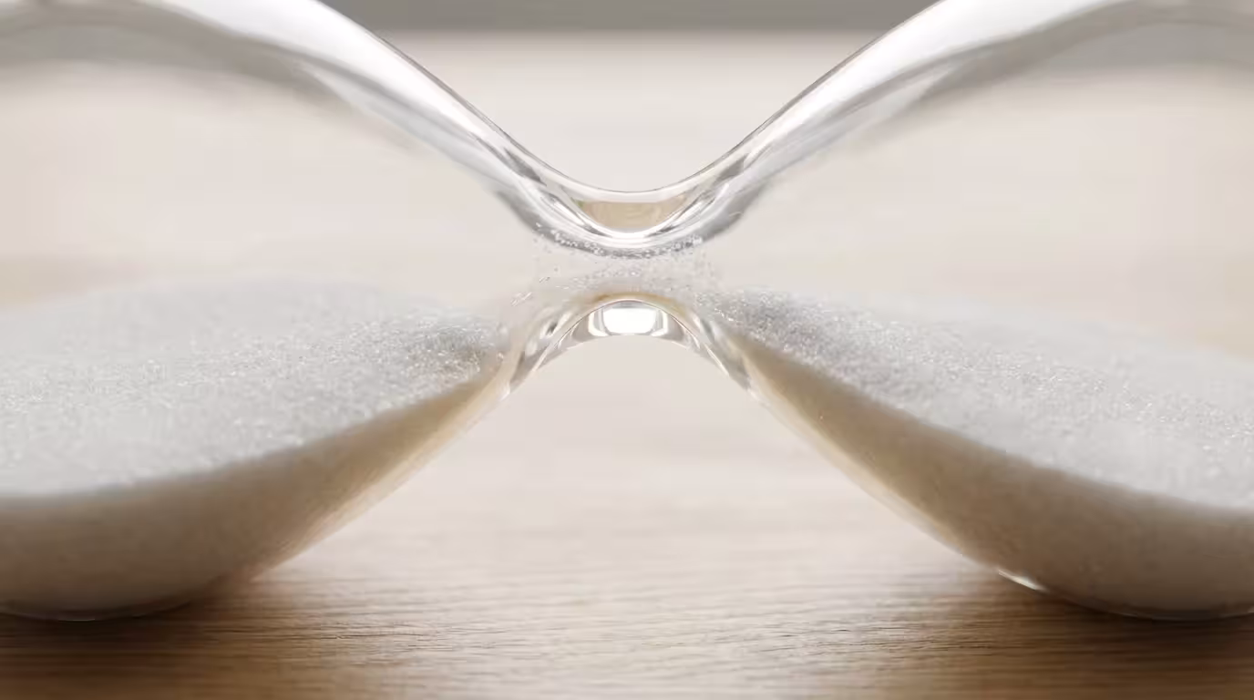 Close-up macro photograph of a modern hourglass with sand flowing to represent time management.