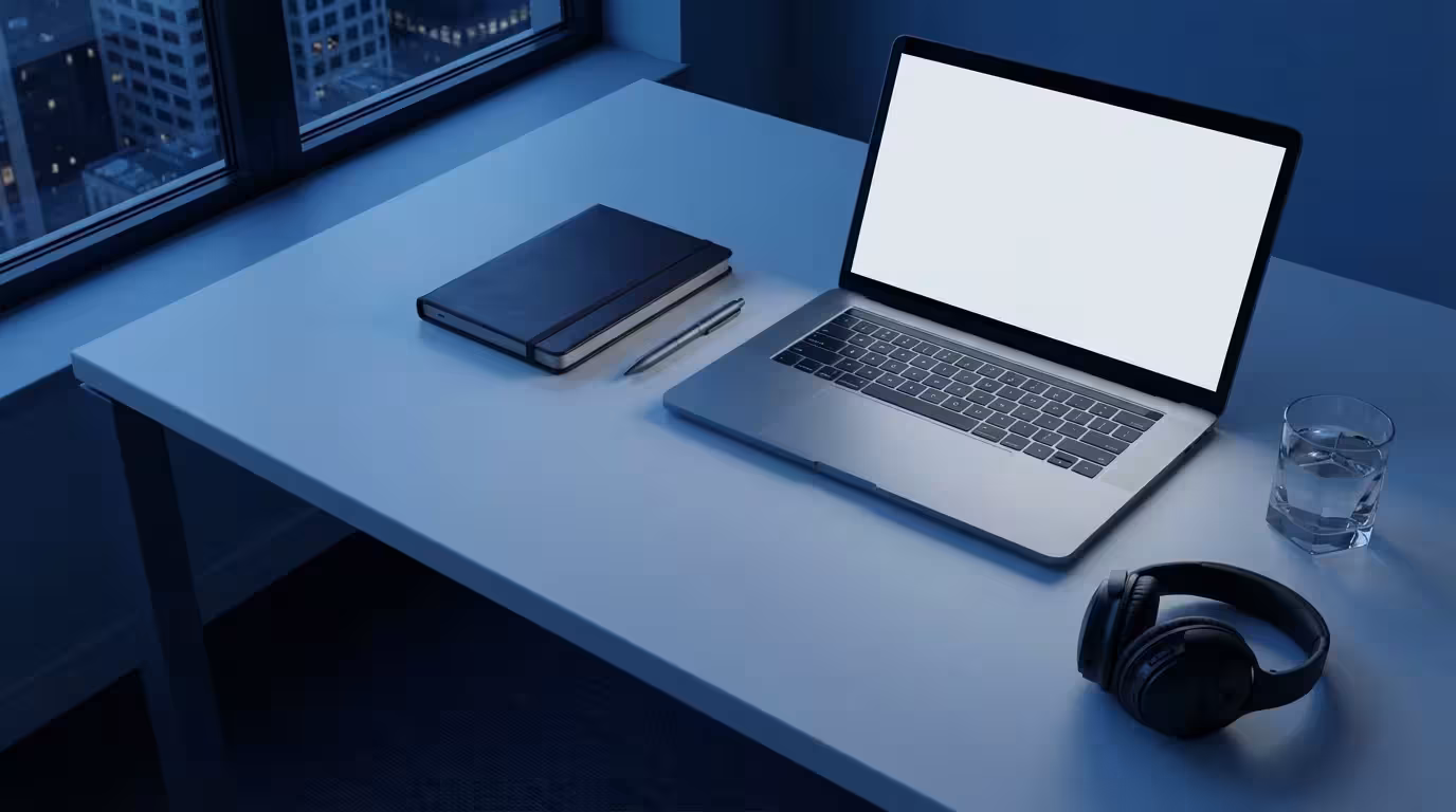 Flat lay of organized office desk with laptop and headphones in cool blue evening lighting.