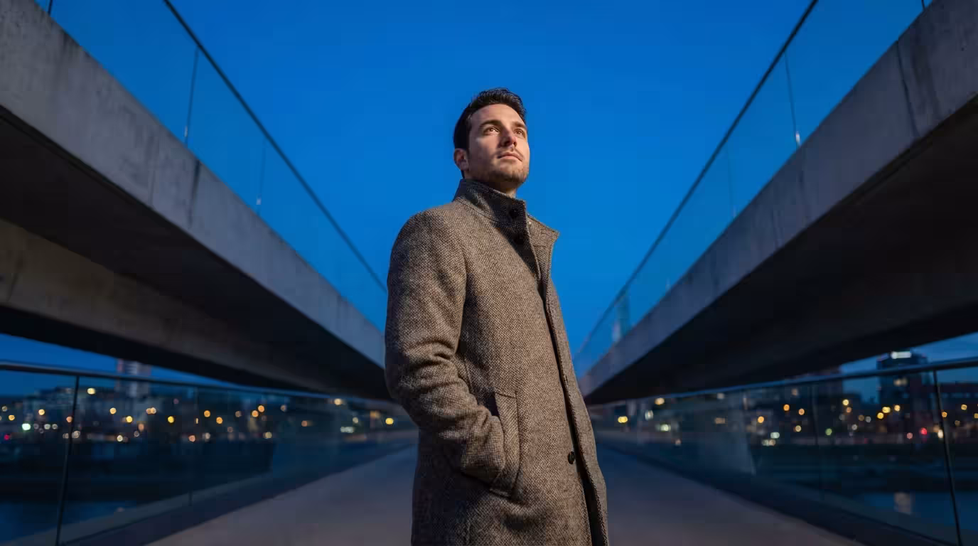 Low angle photo of man on urban bridge at blue hour looking toward horizon.