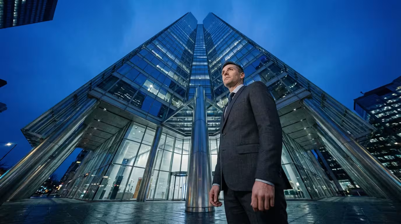 Low angle view of a professional man looking up at a modern skyscraper during blue hour.