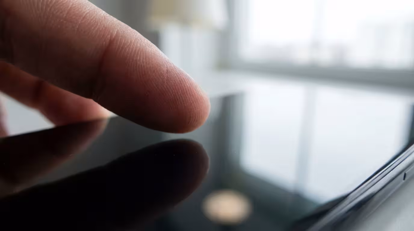 Macro close-up of a thumb pausing over a dark smartphone screen representing mindful hesitation