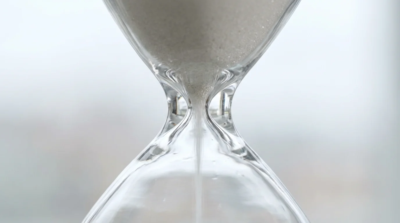 Macro close-up of white sand flowing through a clear glass hourglass.