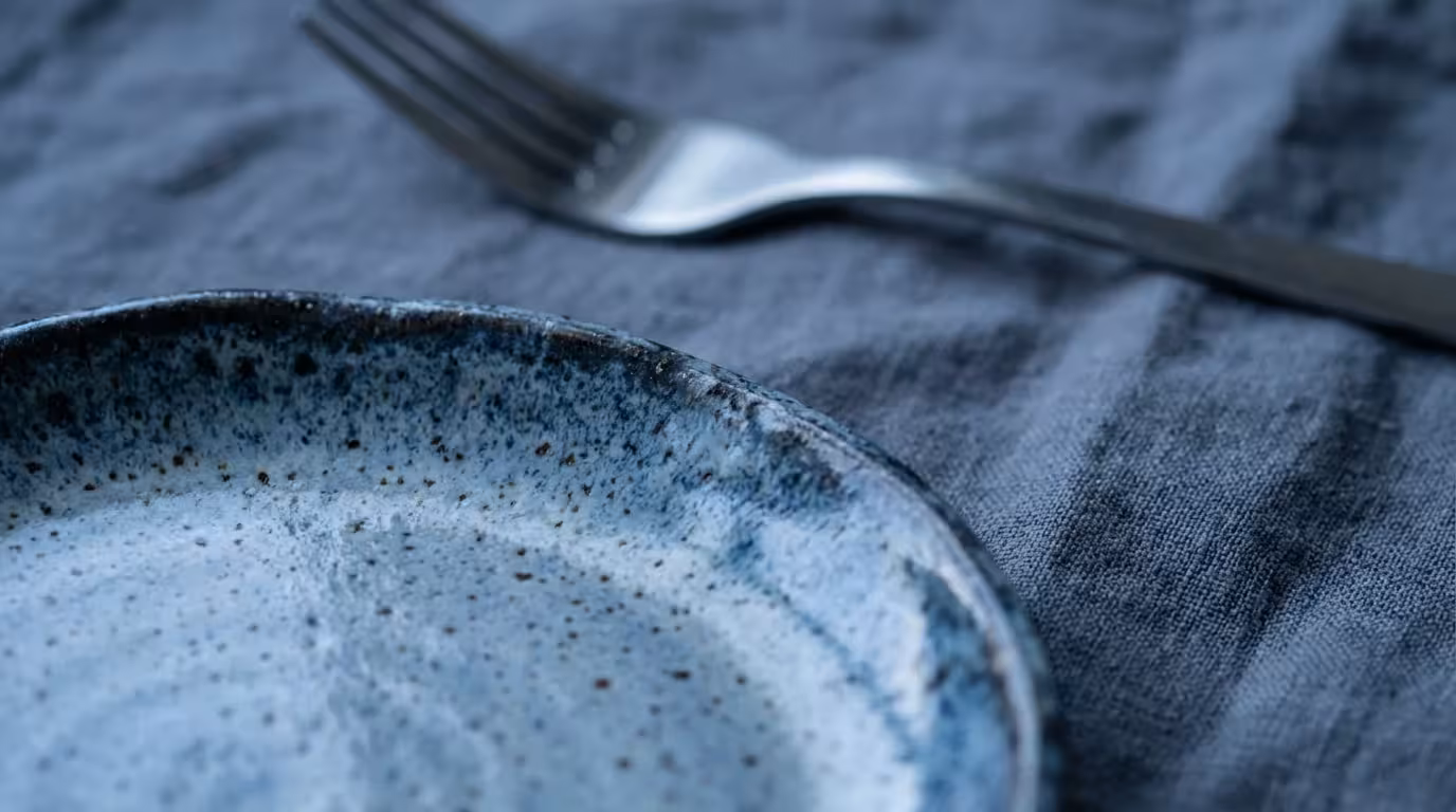 Macro detail of ceramic plate and linen napkin under cool blue evening lighting.