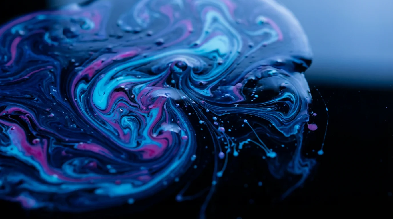 Macro photograph of highly saturated indigo and cyan ink spontaneously blending on a dark surface.