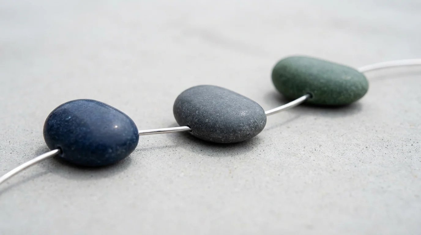 Macro photograph showing three polished stones linked by a silver wire, representing chained habits.