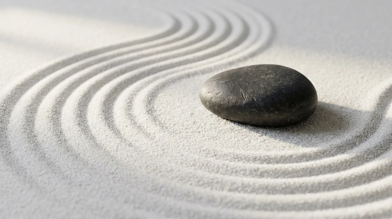Macro photography of raked white sand and a smooth stone in a Zen garden.