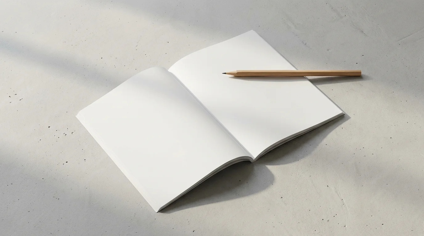 Minimalist flat lay of a thin open paperback book and a single sharp pencil on concrete.