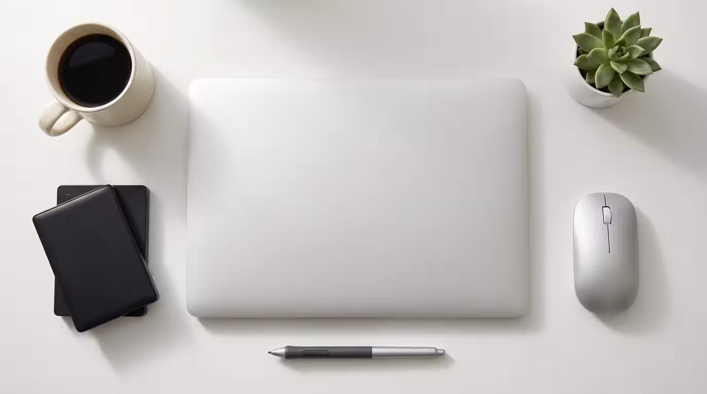 Organized flat lay of closed laptop and tech accessories on a clean white desk.