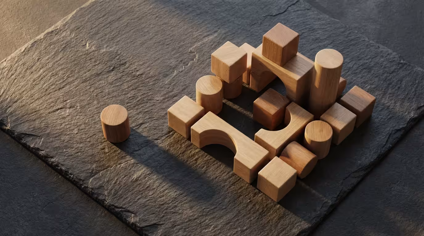 Wooden geometric blocks arranged on a dark slate surface with dramatic afternoon shadows.