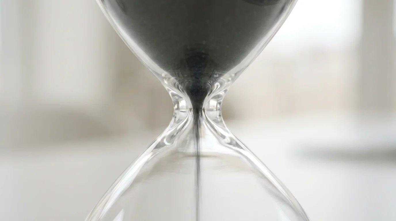 Macro photography of sand falling through a glass hourglass neck symbolizing time constraints.